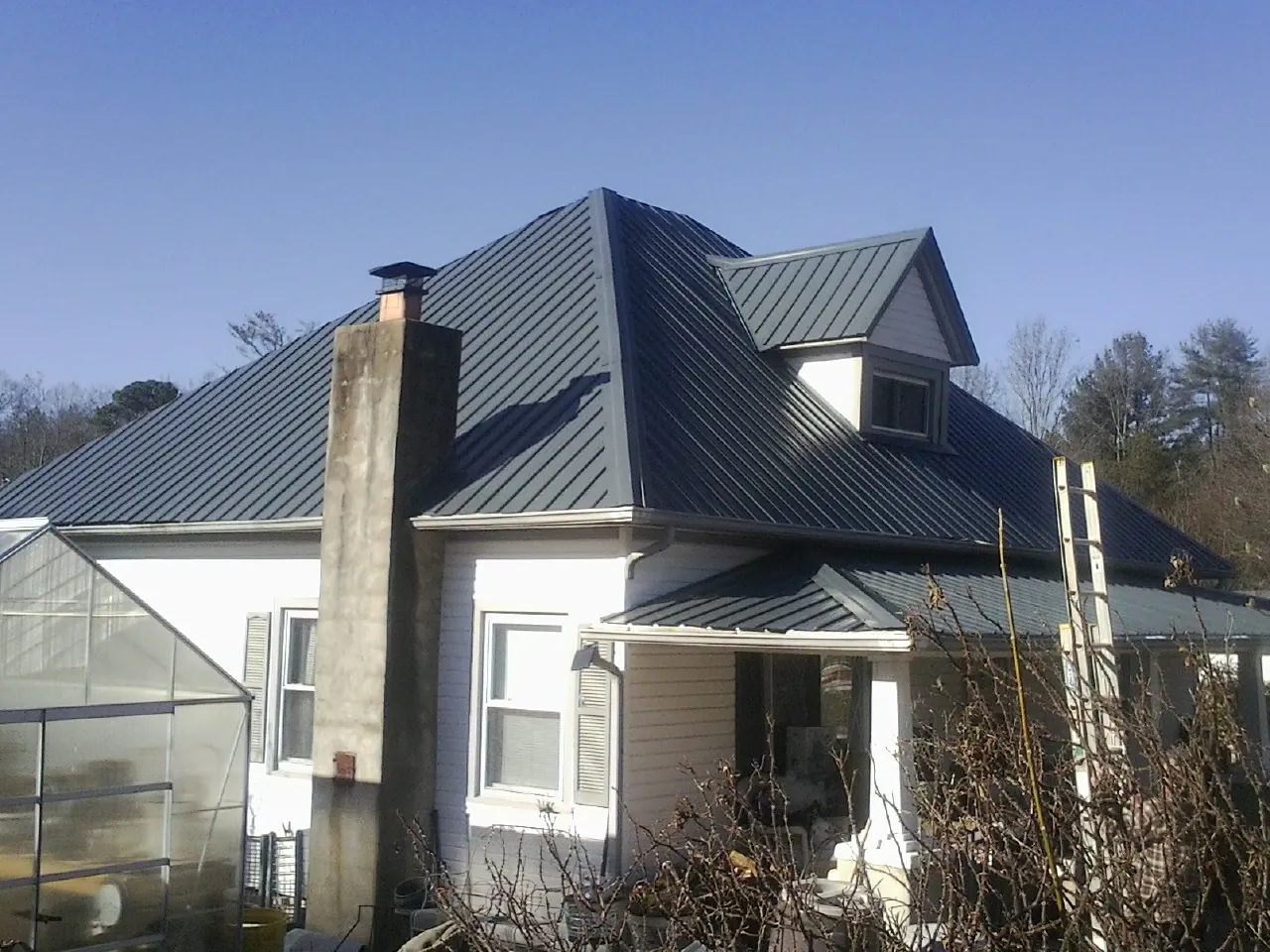 Dark blue standing seam metal roof on a white farmhouse with dormer — Slate & Tile Roof Repair by Roofing Brothers in Madison Heights