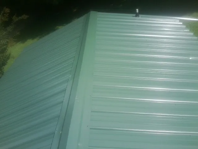 New green metal panels meeting at the ridge of a roof — Flat Roof Repair work by our crew in Madison Heights
